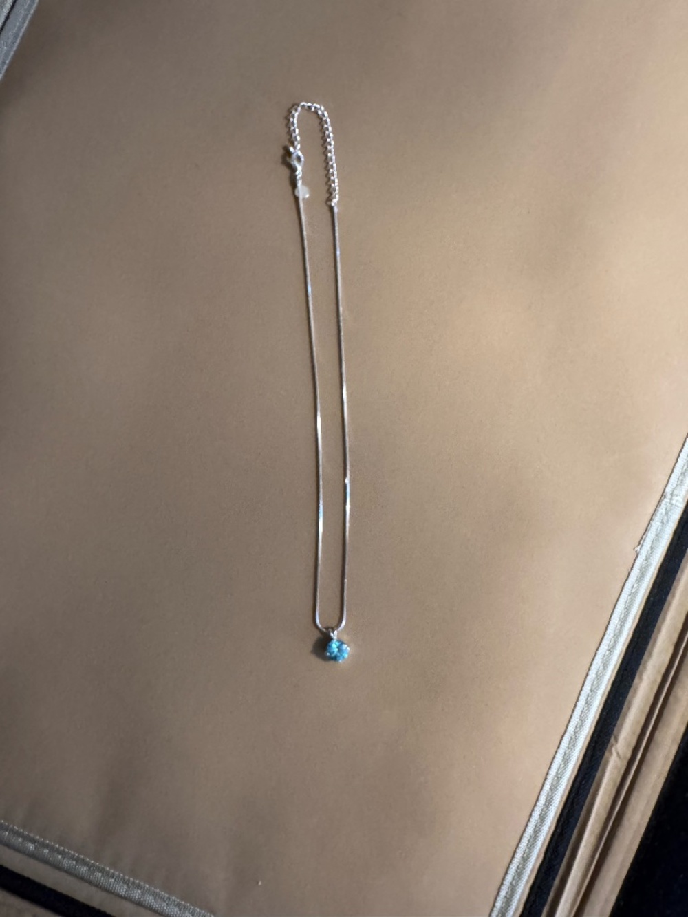 silver snake chain necklace featuring a small blue stone pendant.